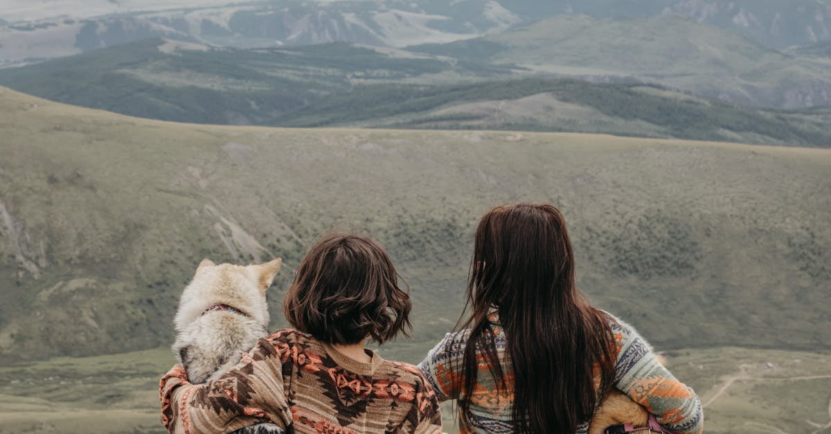 Two women with husky dogs enjoying a panoramic mountain view, capturing adventure and tranquility.